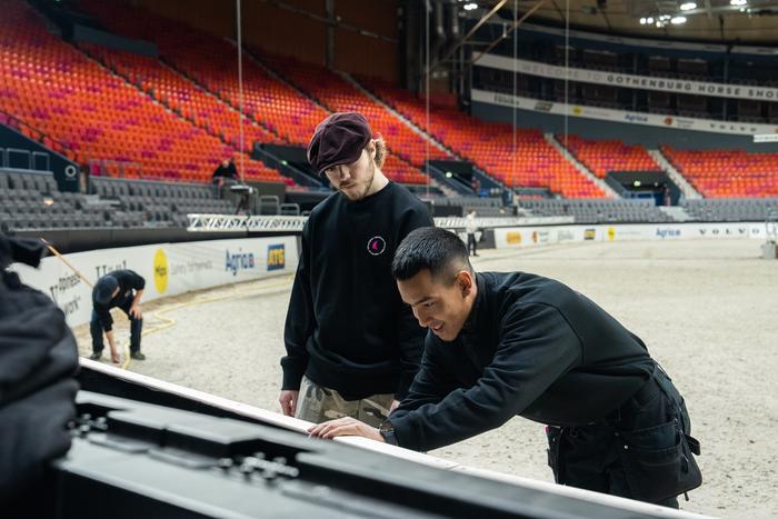 Två montörer hanterar tryckt panel vid arenabarriär i Scandinavium under Gothenburg Horse Show.