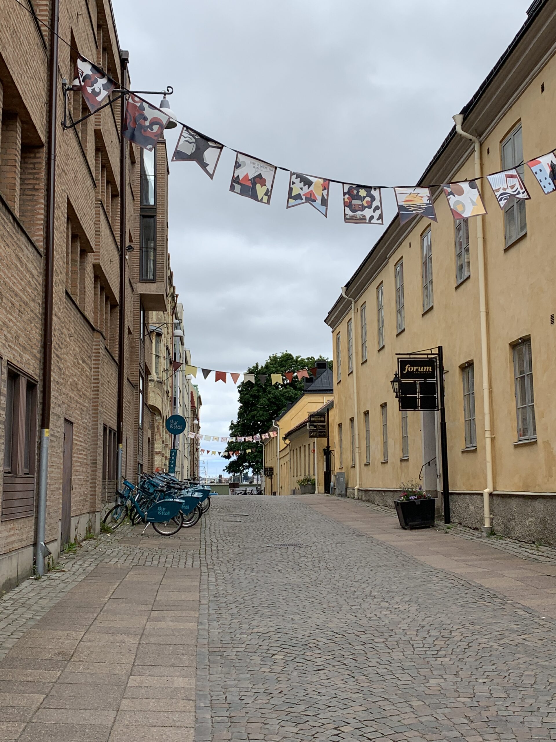 Färgglada trycka fanor hänger längs en gågata mellan byggnader i stadsmiljö.
