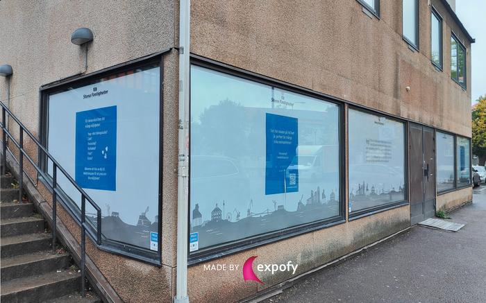 Fönstergrafik på kontorsbyggnad med Stena Fastigheter-budskap, blå grafiska paneler och stadssiluett.