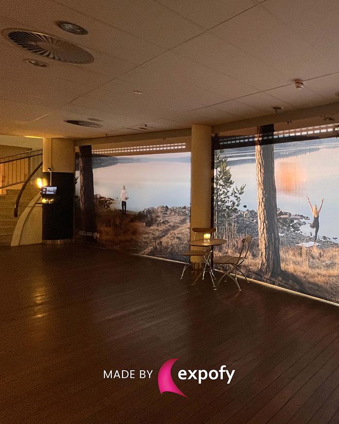 Stora tryckte tygväggar med naturmotiv täcker väggarna i ett hotell- eller konferensrum med parkettgolv.