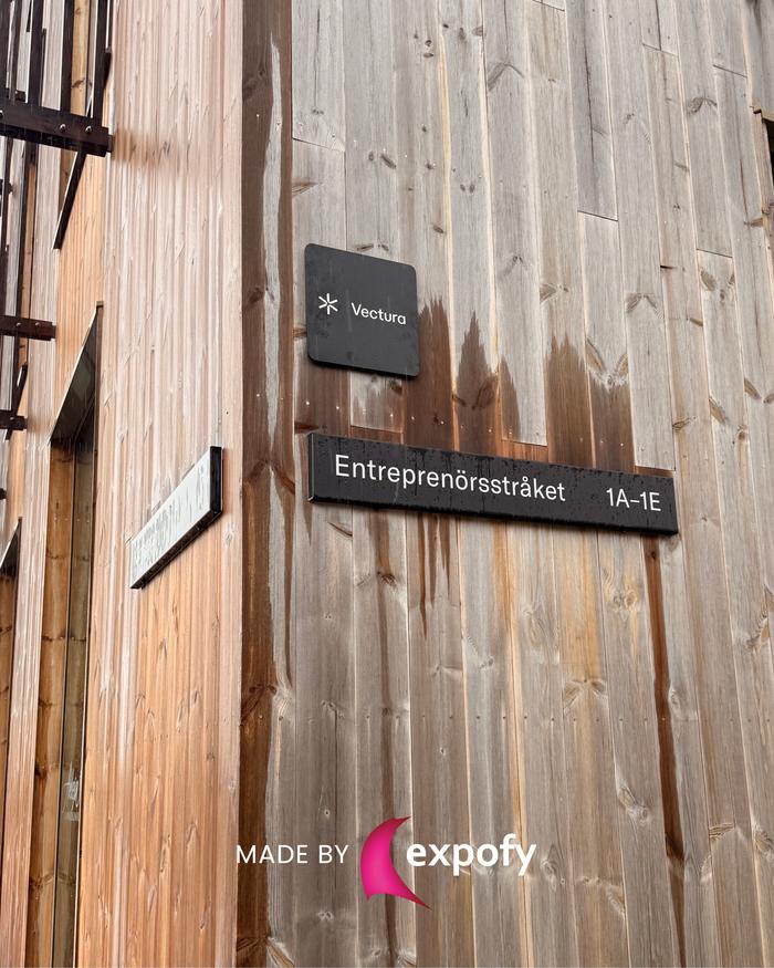 Två mörka skyltar monterade på träfasad – en med Vectura-logotyp och en med adresstexten Entreprenörsstråket 1A–1E