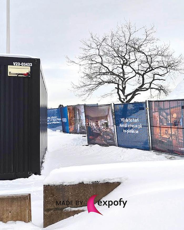 Tygvepor med tryckt text och interiörbilder uppsatta på byggstängsel i vintermiljö