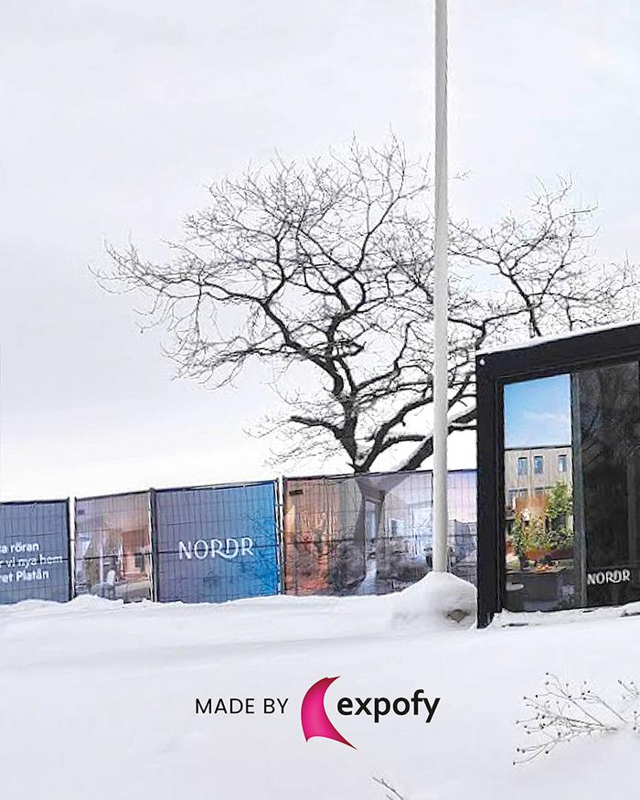 Byggstängsel med tryckt grafik för bostadsprojektet Nordr, fotograferat utomhus i vintermiljö med snö