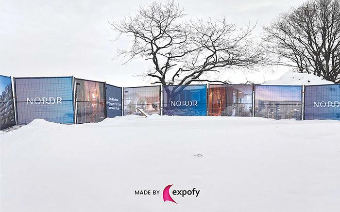 Byggstängsel med tryckt grafik för NORDR, uppställt utomhus i vintermiljö med snö.