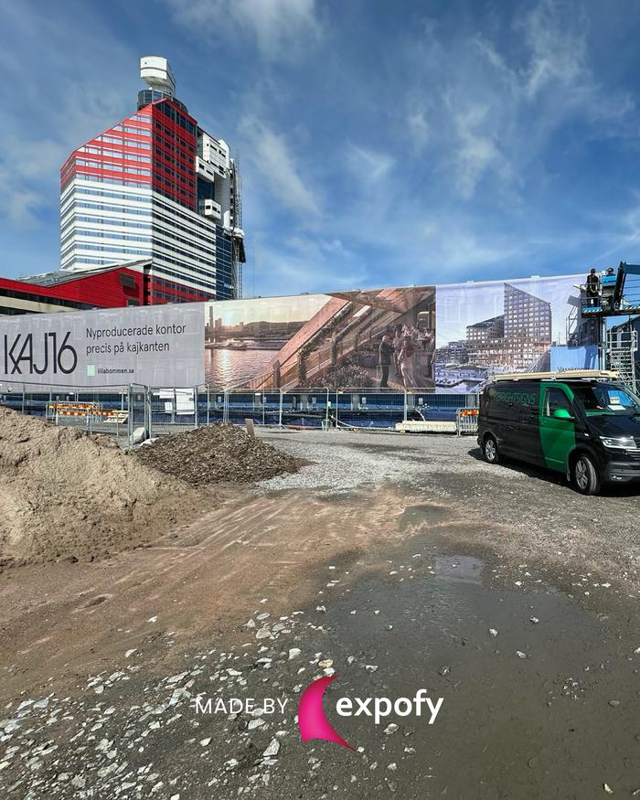 Stor tryckt byggplatsväpa framför höghus visar projektbilder och texten