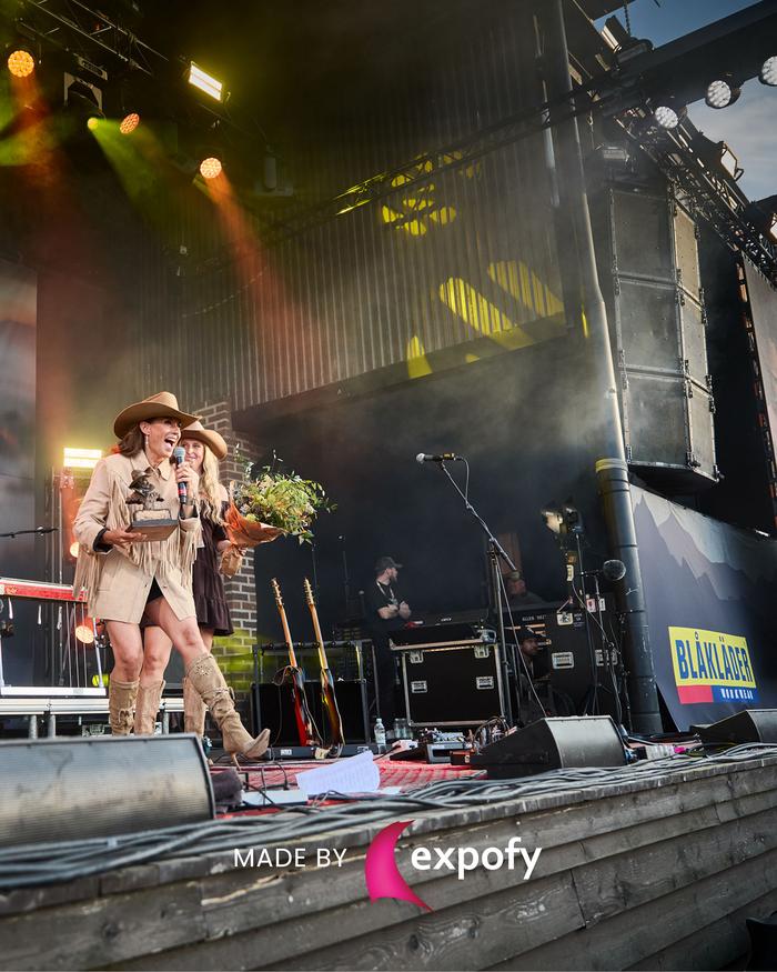 Tryckt scenbakgrund och reklambanderoll med Bläkläder-logotyp på utomhusfestival.