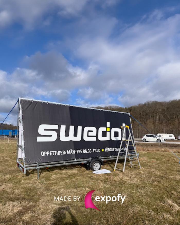 Tygvepa på trailer med tryckt logotyp och öppettider för Swedol, monterad utomhus på gräsplan.