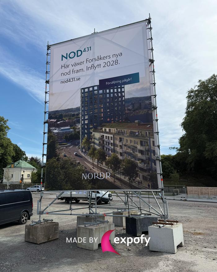 Tygvepa på ställning vid byggarbetsplats med tryckt fasadbild och projektinformation för bostadsprojektet NOD431