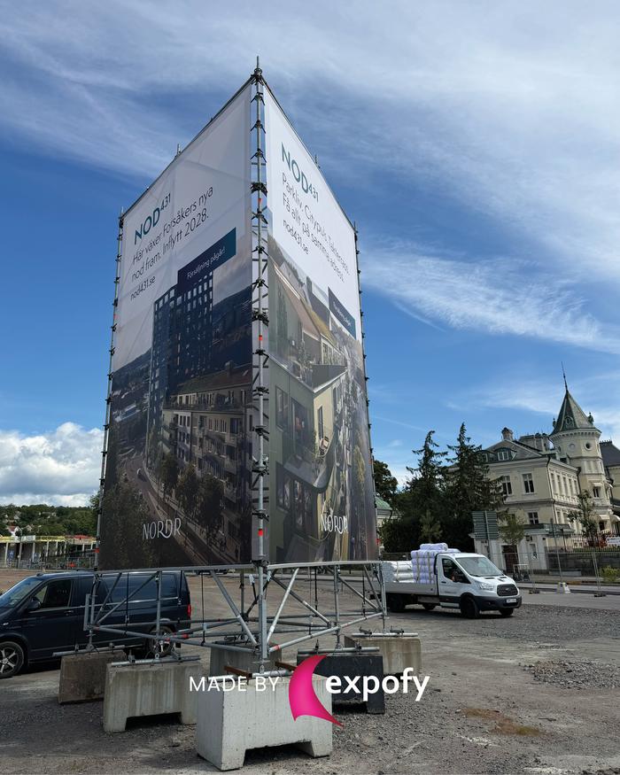 Stor tygvepa på byggnadsställning vid byggarbetsplats, med tryck av text och bilder för bostadsprojektet NOD431