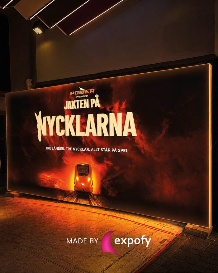 Stor belyst lightbox med filmaffisch för teaterproduktion, monterad som fristående skylt i mörk lokal.