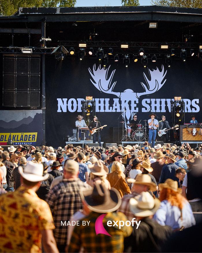 Stor svart scenbakgrund med vit logotyp för Northlake Shivers. Band uppträder på scen framför publik med cowboyhattar.